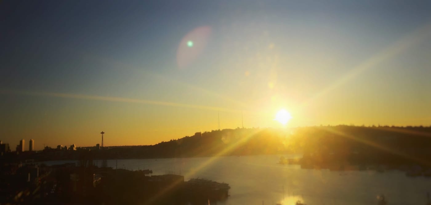 Sun flaring over a dark lake at golden hour.