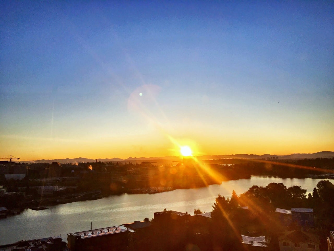 Sunrise flaring over a lake and treetops.