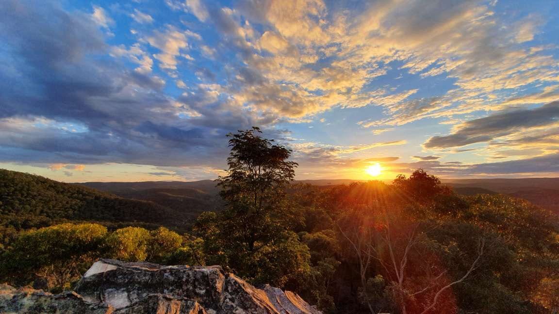 Sun bursting over a valley under streaked clouds.