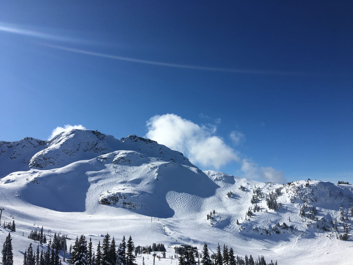 Fresh snow on a craggy mountain under blue sky.