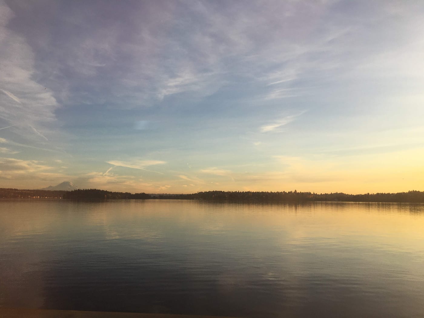Mount Rainier faint over calm water at dusk.